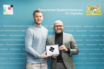 Manuel Neuer und Digitalminister Dr. Fabian Mehring halten gemeinsam ein Tablet, auf dem das BayCode Logo zu sehen ist.